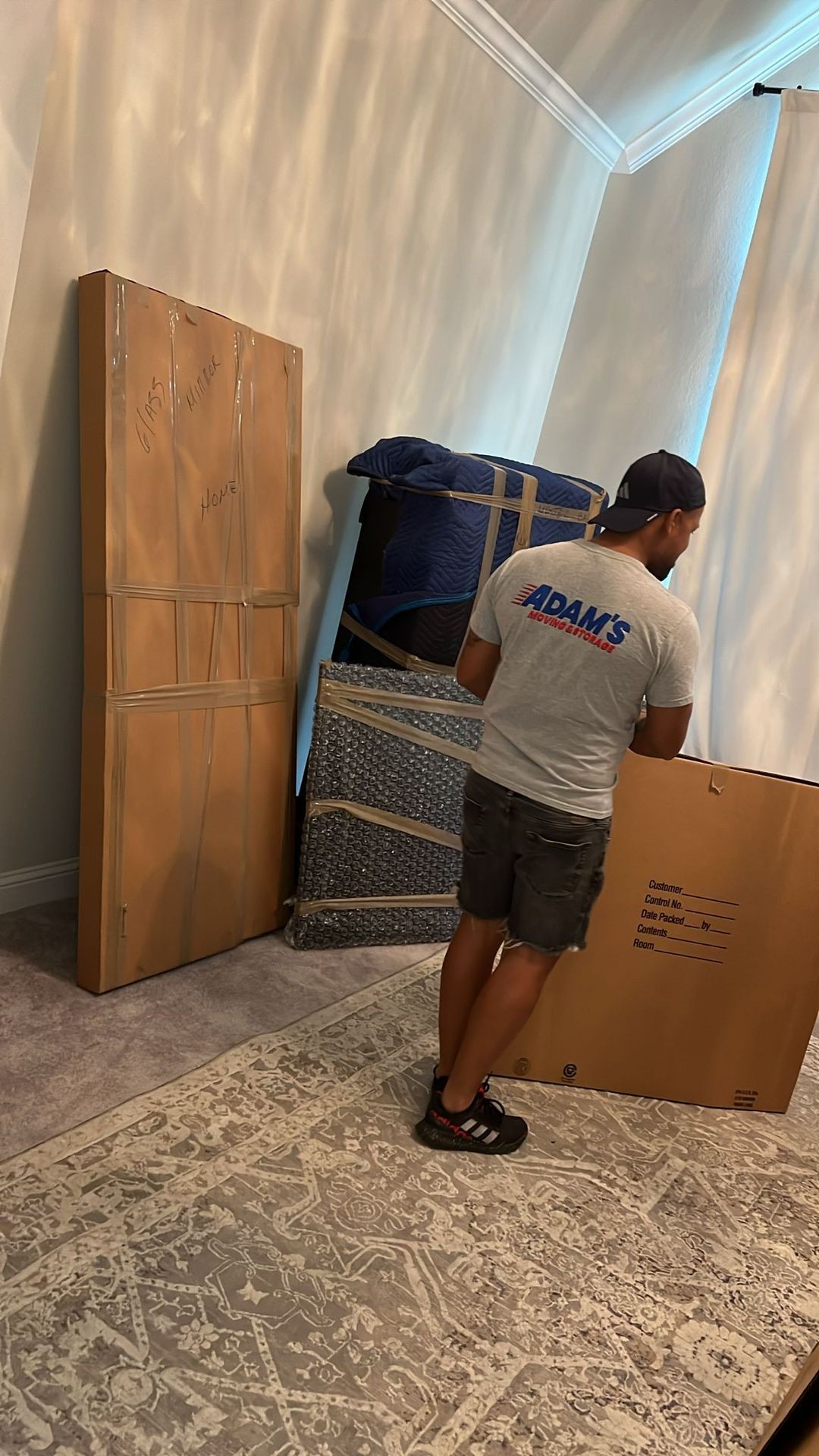 Moving company worker standing beside packed furniture and boxes in a room.