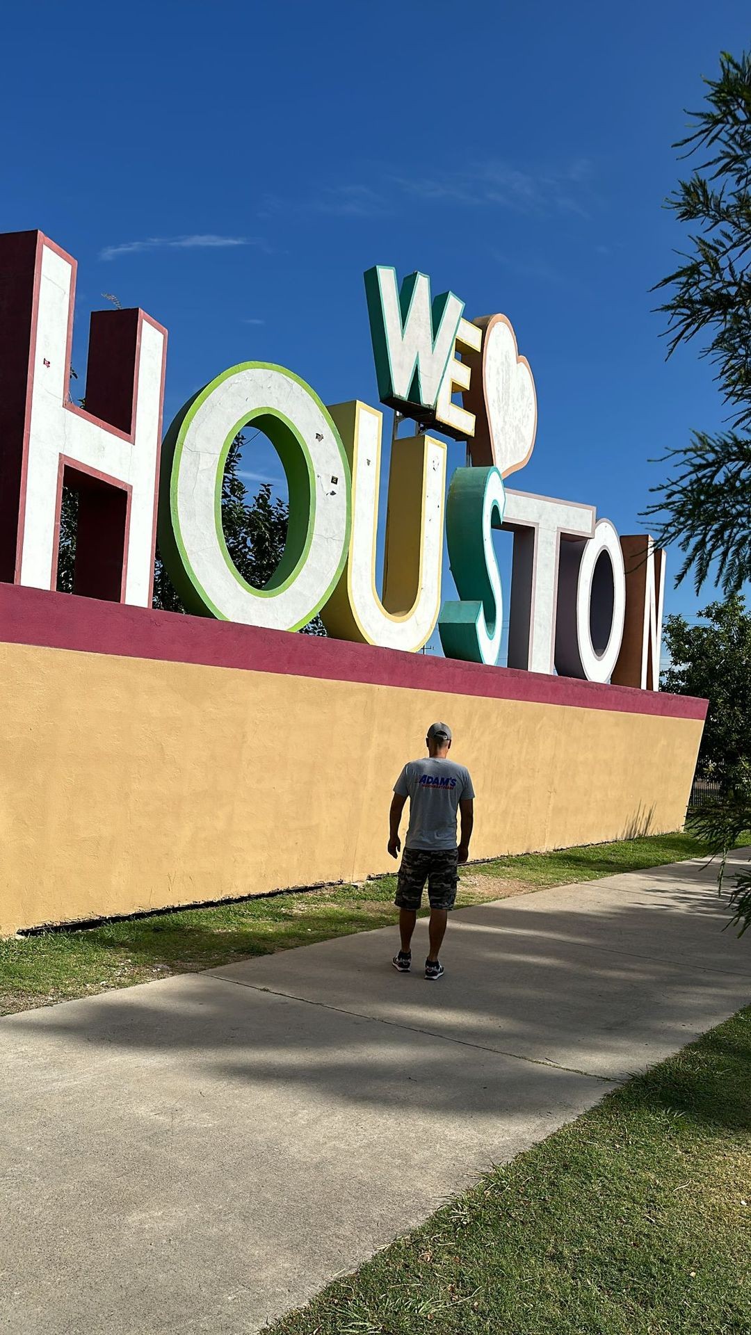 Person walking towards a large colorful 'We Heart Houston' sign on a sunny day.